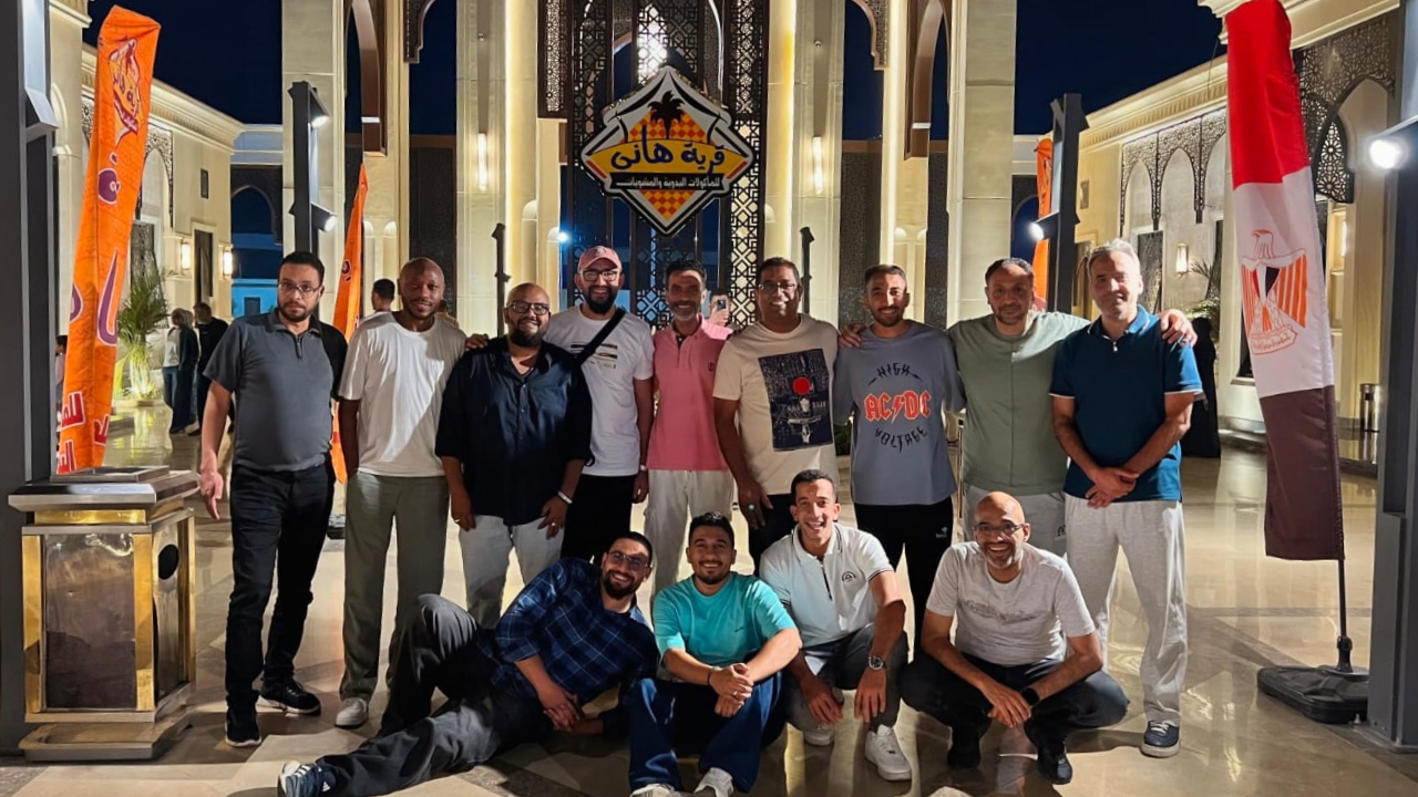 The AxessAll Egypt team outside Hany Village at night, standing in a row with four colleagues crouching in front, beneath the venue's illuminated sign.