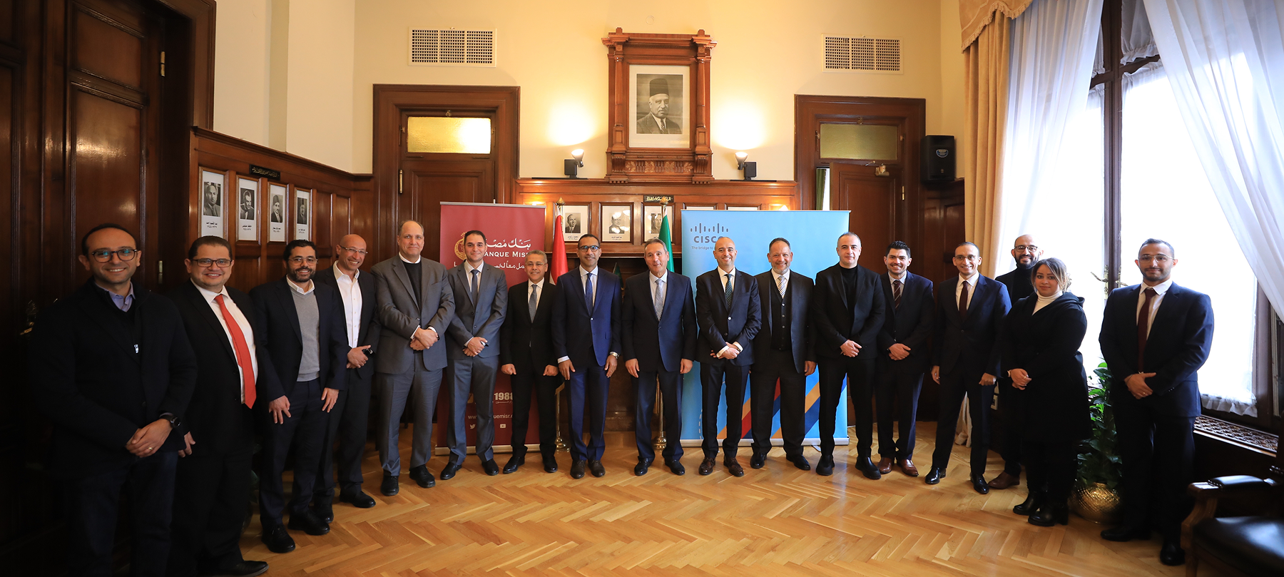 Representatives of Banque Misr, Cisco and AxessAll standing together in a wood-panelled hall, with Banque Misr and Cisco banners behind them.